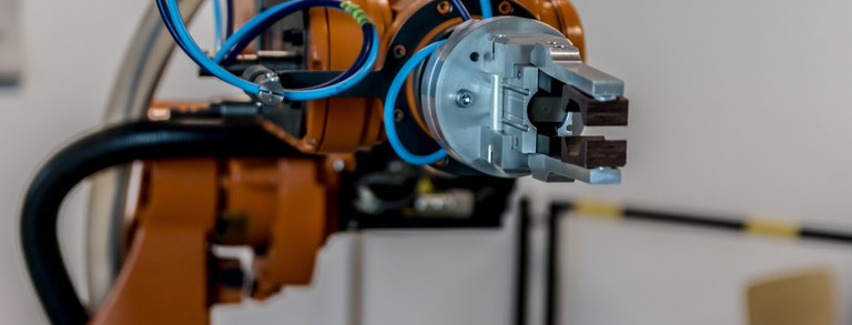 Roboterarm Zu sehen ist ein orangener Roboterarm mit einer Greifzange die an mehrere Schläuche gebunden ist.