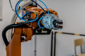 Zu sehen ist ein orangener Roboterarm mit einer Greifzange die an mehrere Schläuche gebunden ist.