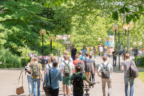 Studierende laufen über den Campus Nord. Es ist eine große rote Skulptur in Form von großen Zahnrädern zu erkennen.